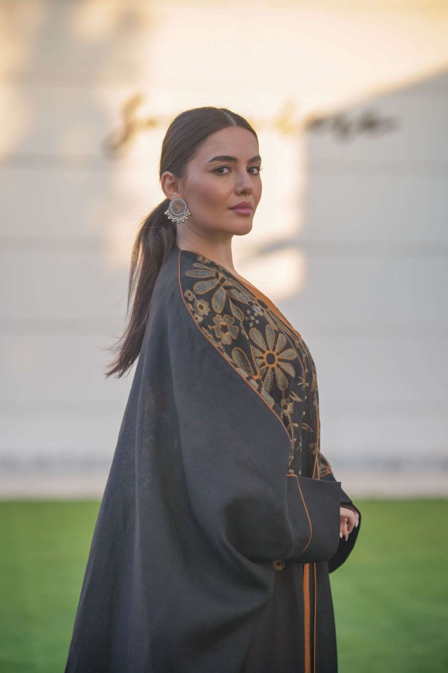 Elegant black bisht with golden floral embroidery and wide sleeves layered over a rust-colored jumpsuit