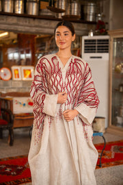 Woman wearing beige bisht with bold red embroidery on shoulders and sleeves called Crimson Bloom in cozy indoor setting