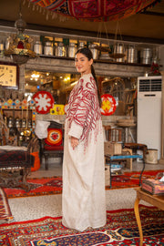 Woman wearing beige bisht with bold red embroidery on shoulders and sleeves called Crimson Bloom in cozy indoor setting