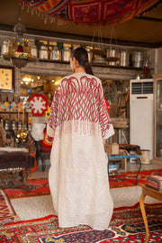 Woman wearing beige bisht with bold red embroidery on shoulders and sleeves called Crimson Bloom in cozy indoor setting