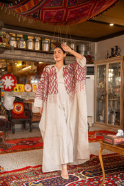 Woman wearing beige bisht with bold red embroidery on shoulders and sleeves called Crimson Bloom in cozy indoor setting