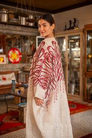 Woman wearing beige bisht with bold red embroidery on shoulders and sleeves called Crimson Bloom in cozy indoor setting