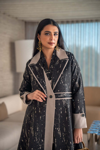 woman wearing elegant black and beige patterned Ashira abaya holding tan handbag in modern living room