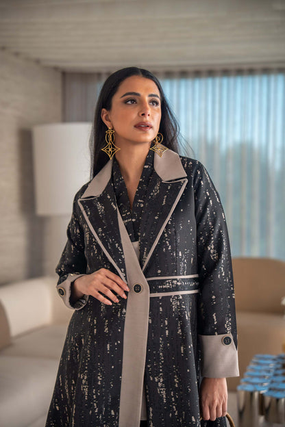 woman wearing elegant black and beige patterned Ashira abaya holding tan handbag in modern living room