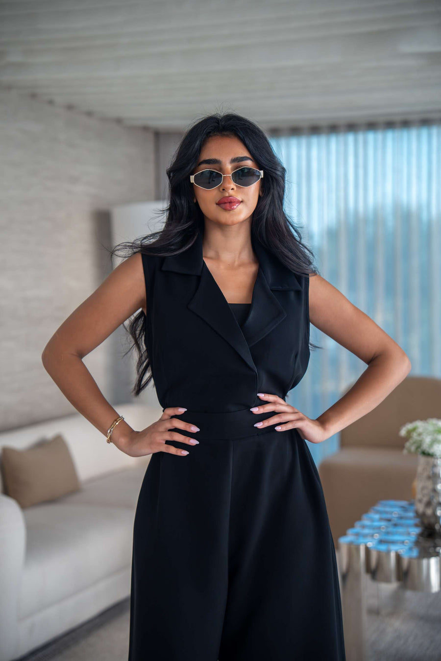 Woman wearing elegant black crepe jumpsuit with sleeveless tailored design and sunglasses indoors