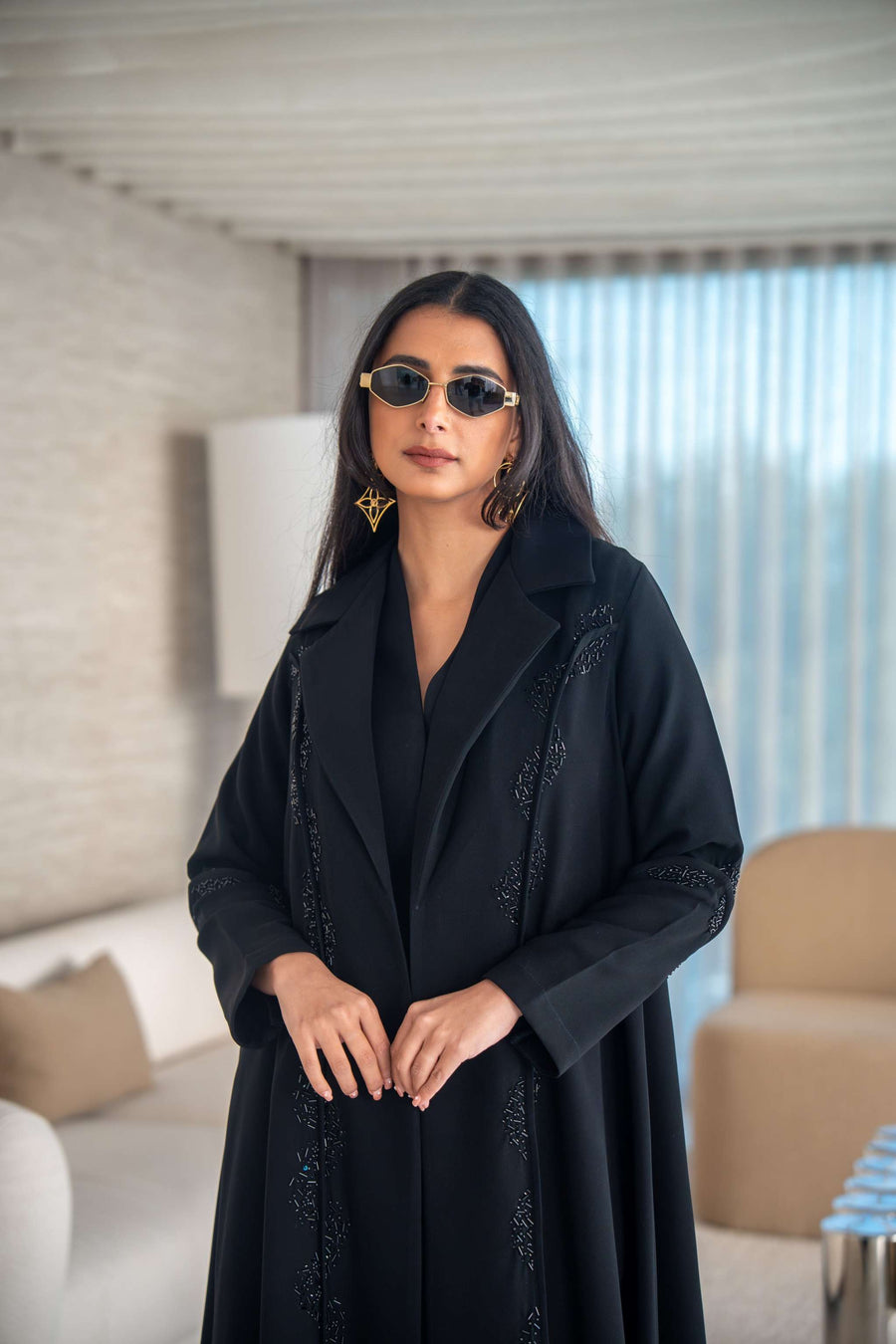 woman wearing elegant black crepe abaya with flowing silhouette and sunglasses indoors