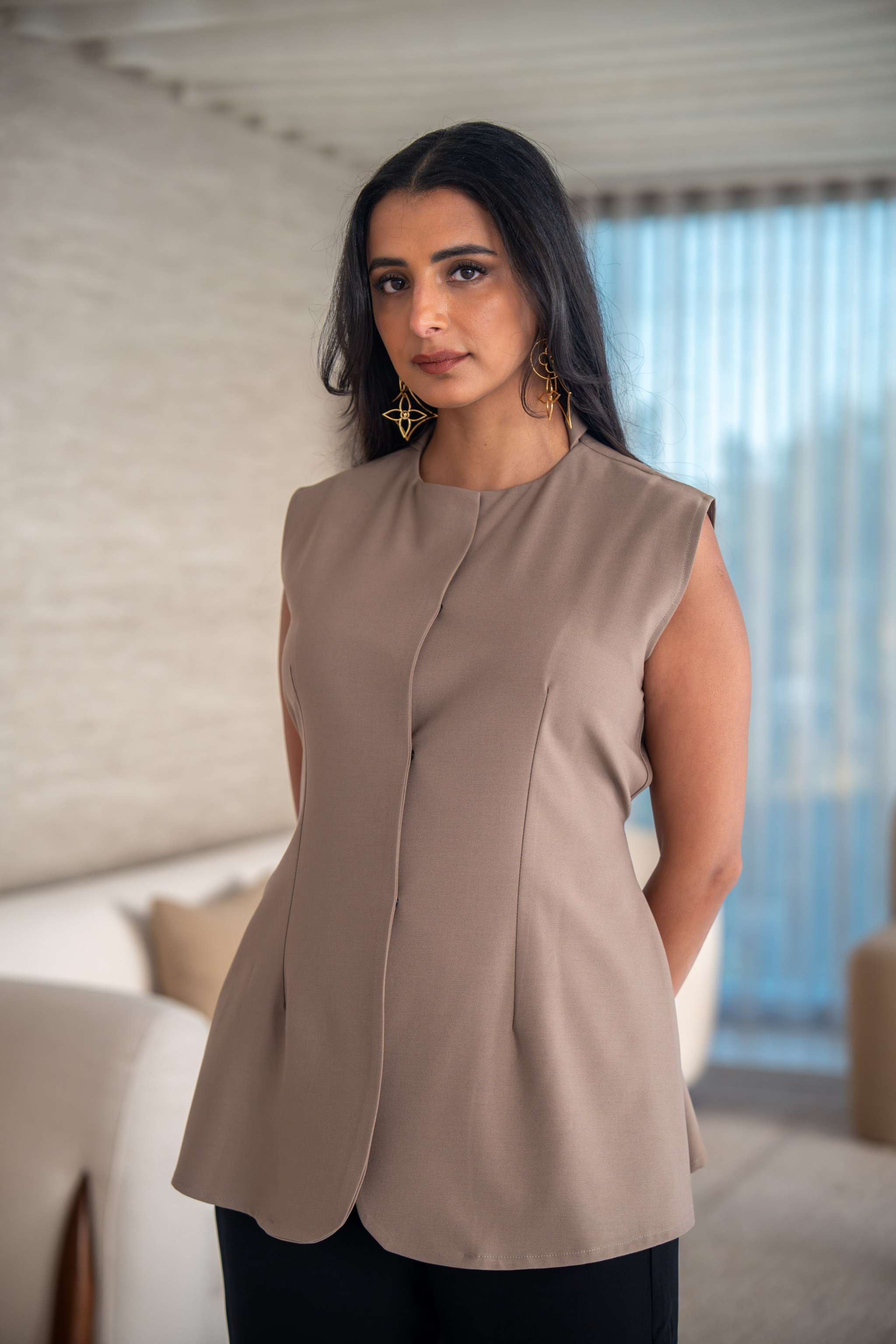 Woman wearing sleeveless beige crepe blouse with hidden front button closure and subtle paneling indoors