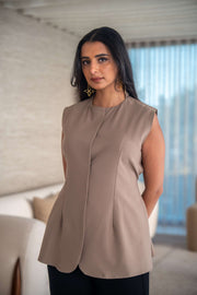 Woman wearing sleeveless beige crepe blouse with hidden front button closure and subtle paneling indoors