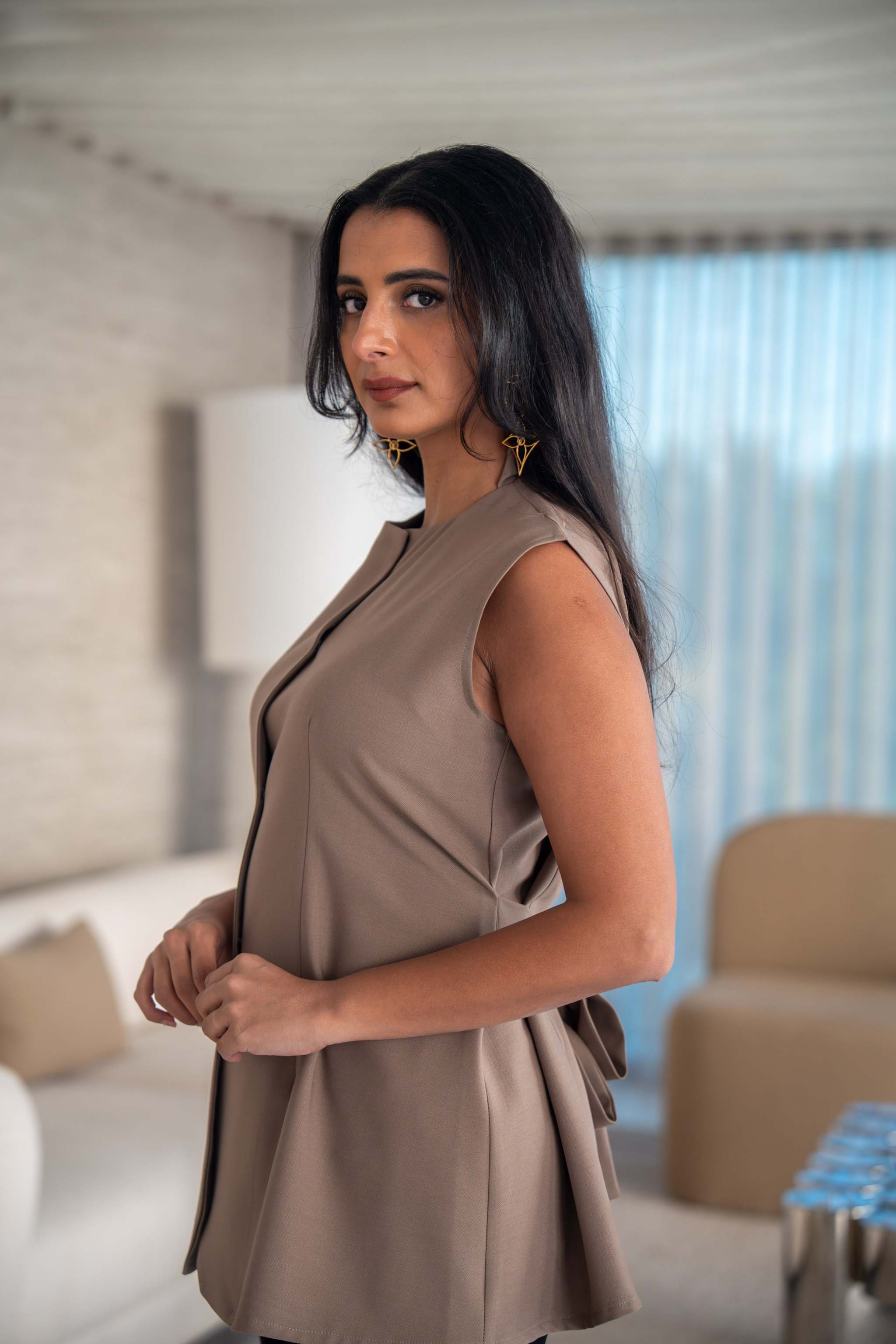 Woman wearing a sleeveless beige crepe vest in a modern indoor setting