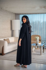 Elegant black crepe abaya with soft, flowing silhouette worn by woman indoors