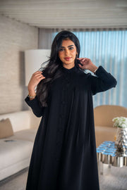 Elegant black crepe abaya with soft, flowing silhouette worn by woman indoors