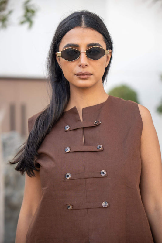 Sleeveless brown blouse with asymmetric button detailing and notched neckline worn by a woman with sunglasses