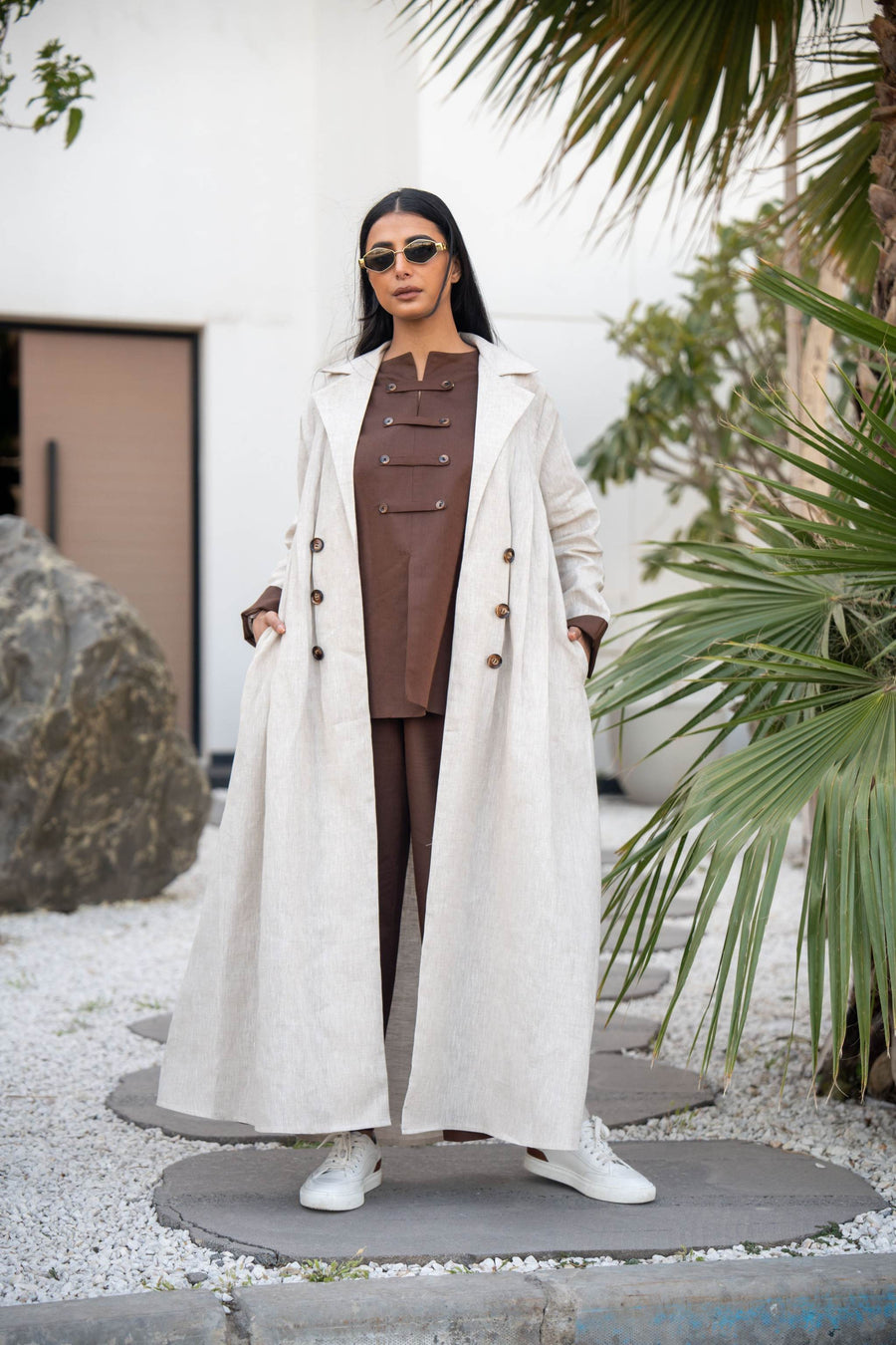 Woman wearing creme chocolate abaya with an elegant long beige coat and sunglasses outdoors