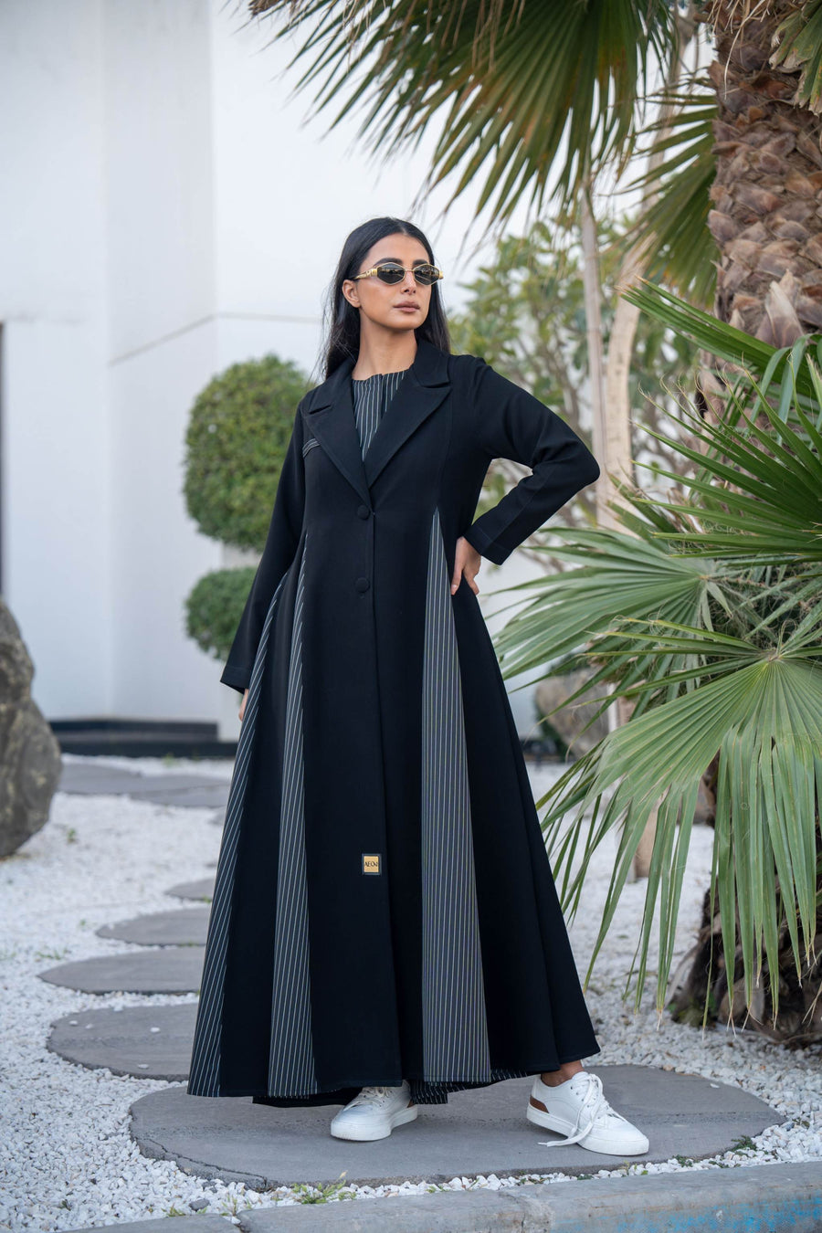 Woman wearing black Crepe Edge abaya with striped crepe details and white sneakers outdoors