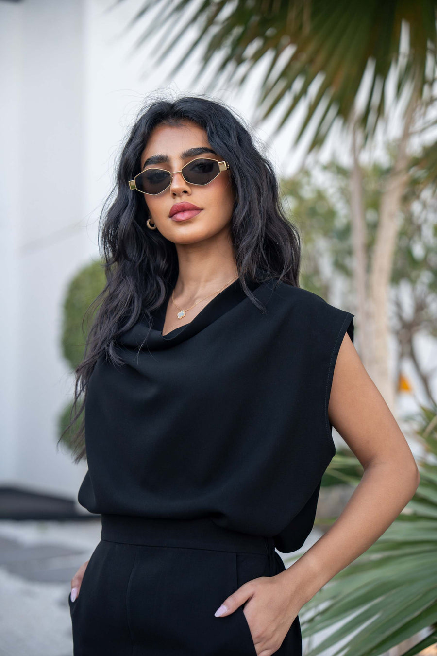 Woman wearing a black crepe blouse with a draped neckline and sleeveless design outdoors.