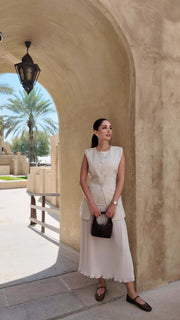 Sleeveless beige Sandy Pleats dress with tailored bodice, front buttons, cinched waist, and soft pleated skirt perfect for warm-weather occasions.