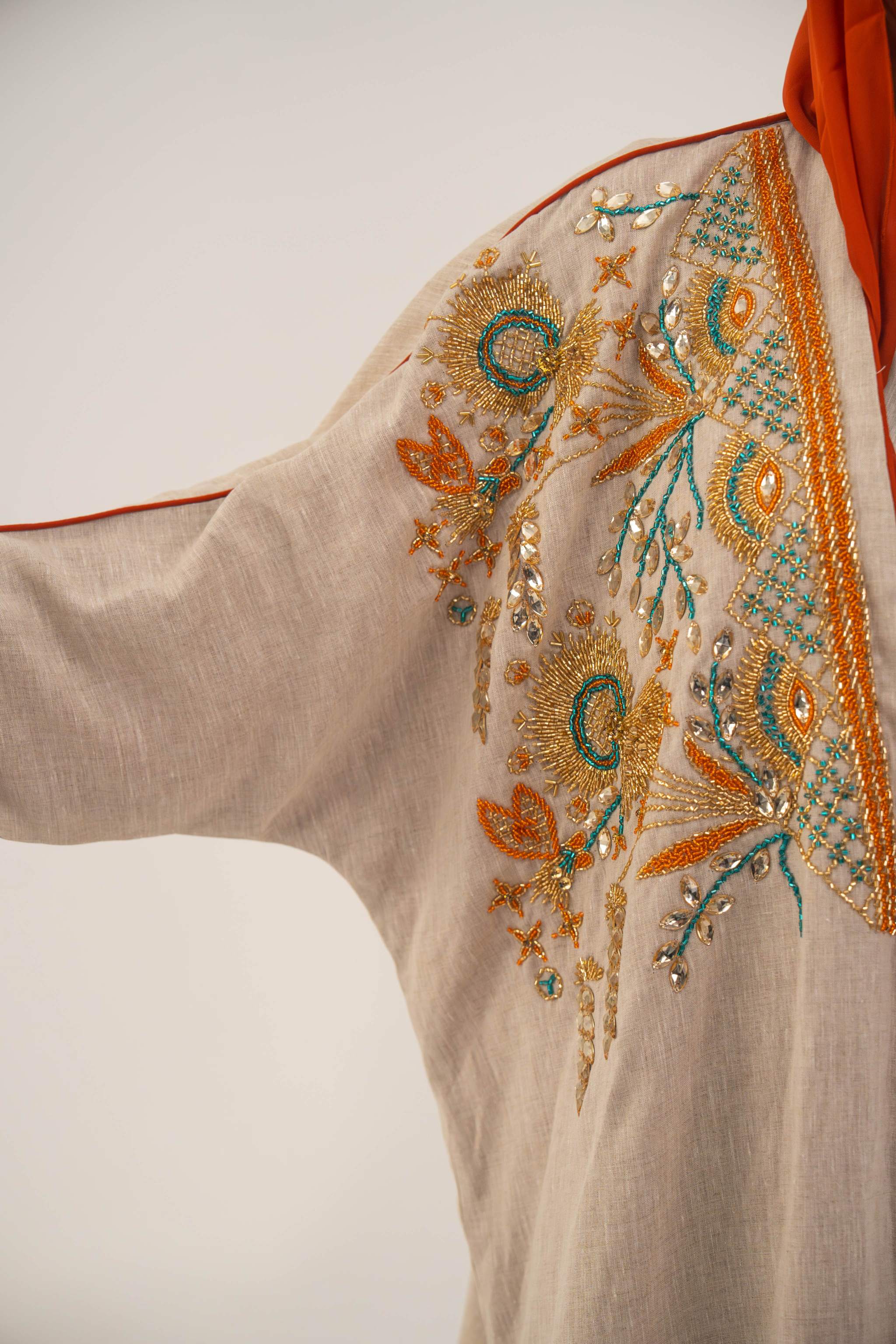 Woman wearing neutral linen Mango Bisht with mango-orange accents and hand-embroidered shoulder panels in earthy and teal tones.