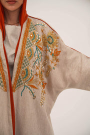 Woman wearing neutral linen Mango Bisht with mango-orange accents and hand-embroidered shoulder panels in earthy and teal tones.