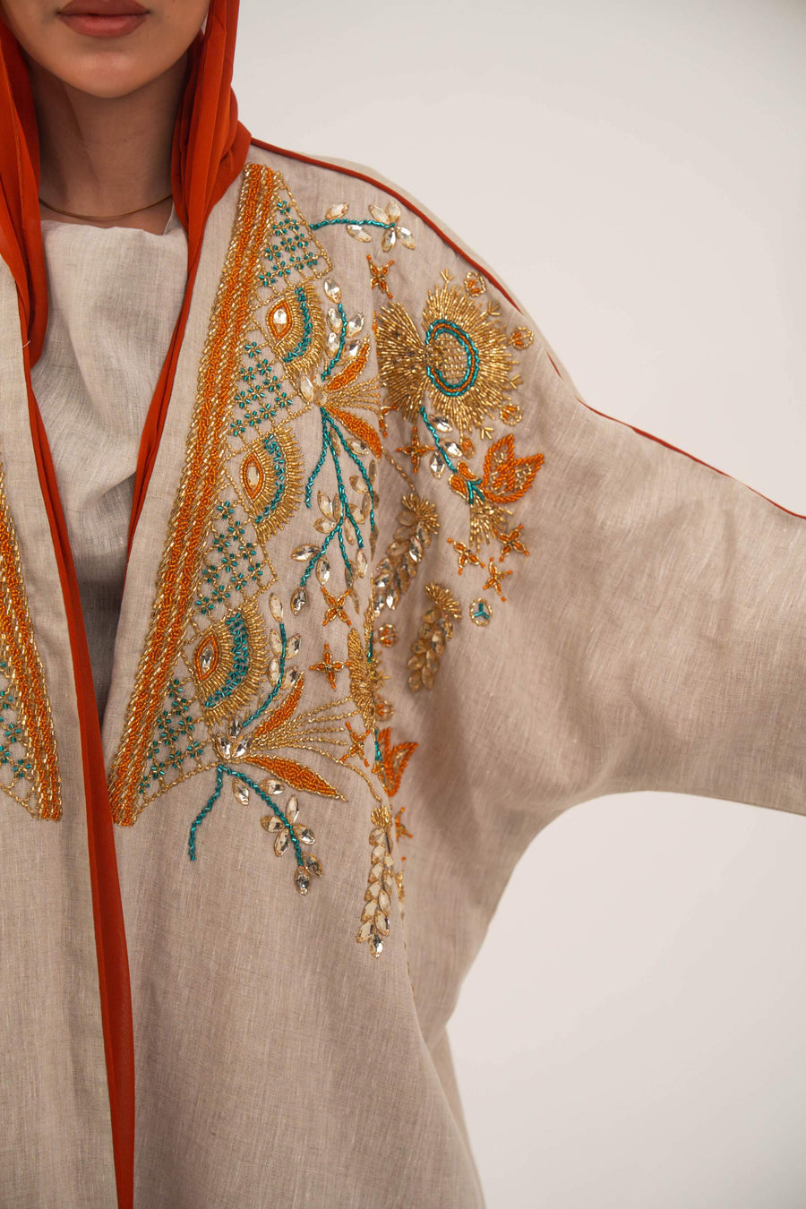 Woman wearing neutral linen Mango Bisht with mango-orange accents and hand-embroidered shoulder panels in earthy and teal tones.