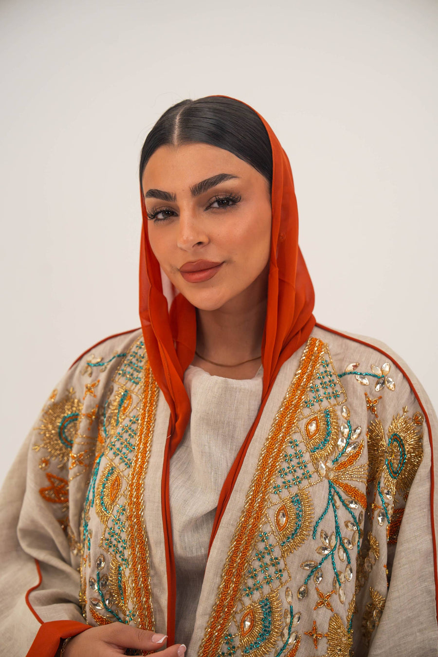 Woman wearing neutral linen Mango Bisht with mango-orange accents and hand-embroidered shoulder panels in earthy and teal tones.