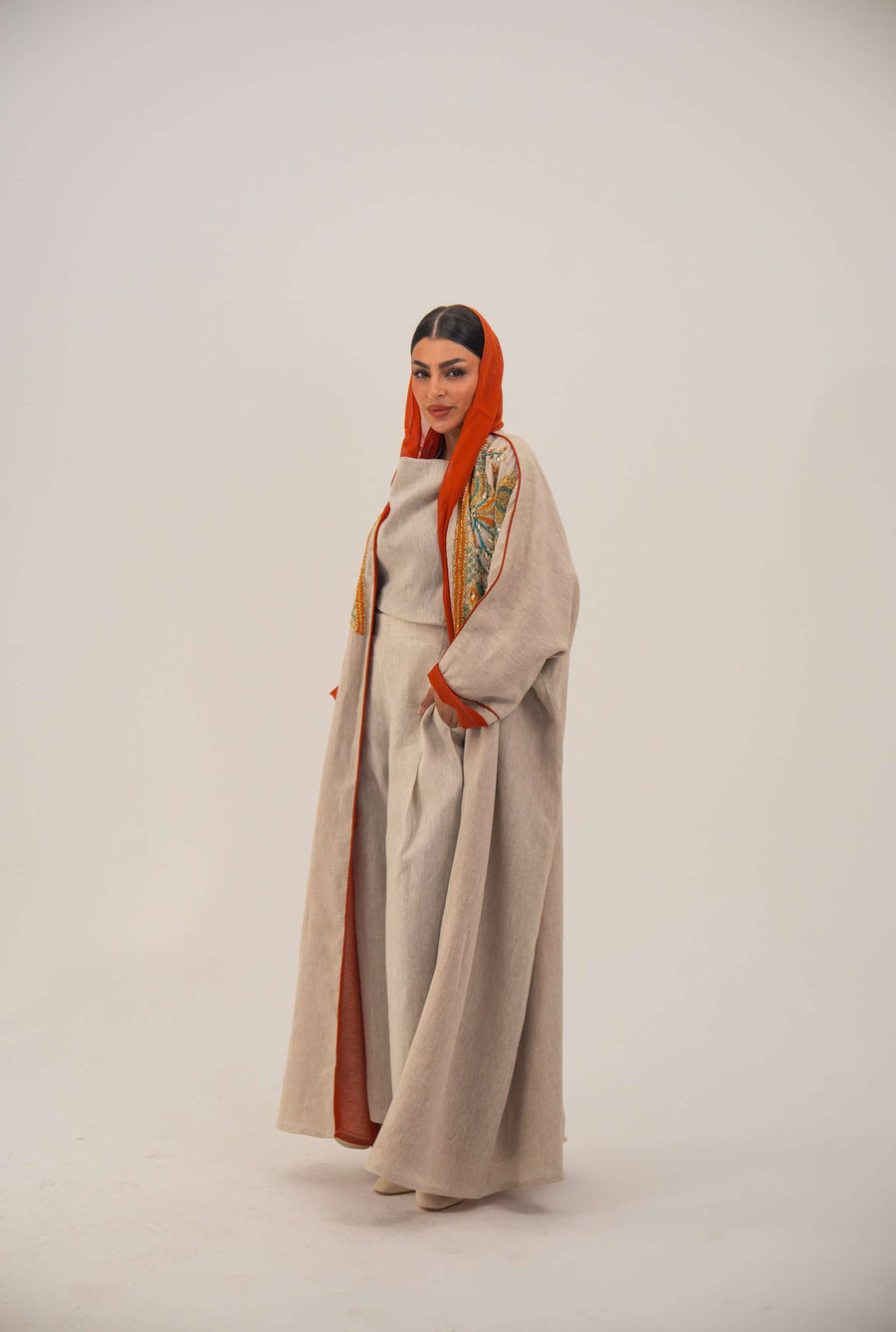 Woman wearing neutral linen Mango Bisht with mango-orange accents and hand-embroidered shoulder panels in earthy and teal tones.
