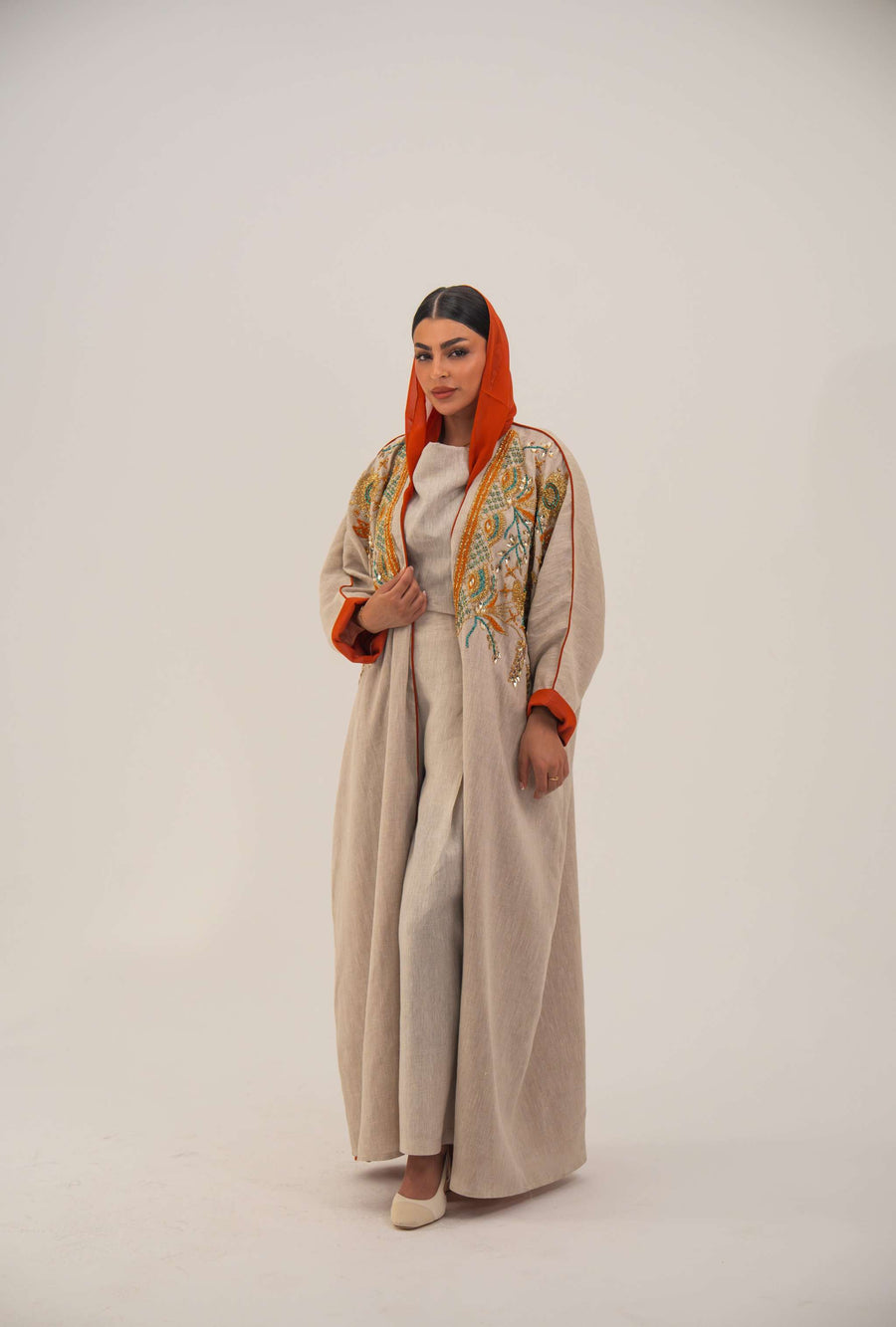 Woman wearing neutral linen Mango Bisht with mango-orange accents and hand-embroidered shoulder panels in earthy and teal tones.