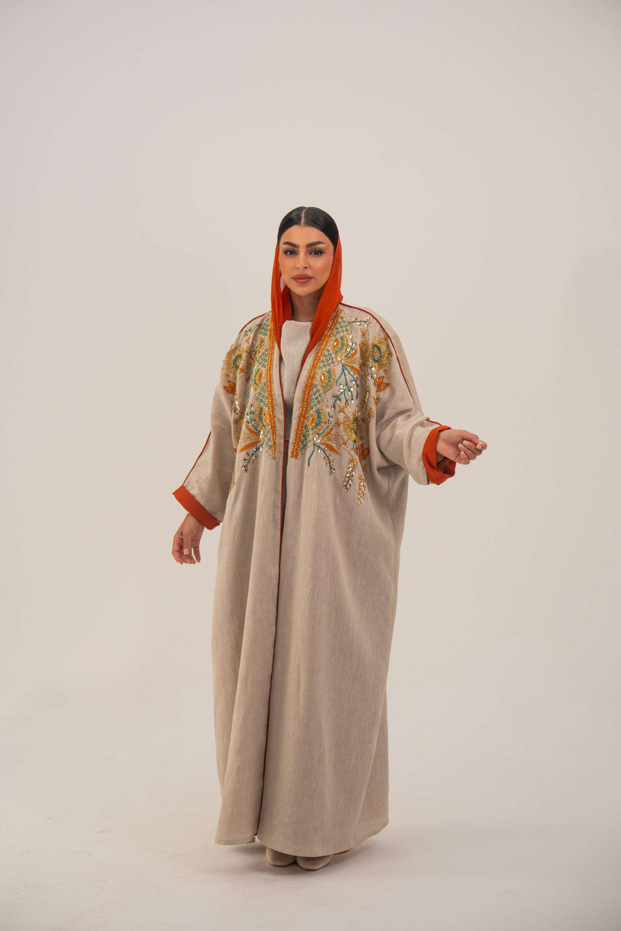 Woman wearing neutral linen Mango Bisht with mango-orange accents and hand-embroidered shoulder panels in earthy and teal tones.