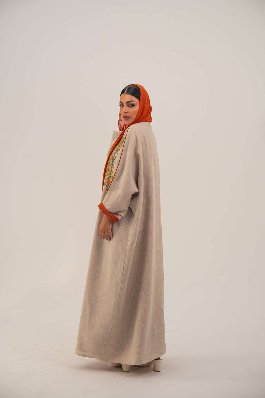 Woman wearing neutral linen Mango Bisht with mango-orange accents and hand-embroidered shoulder panels in earthy and teal tones.