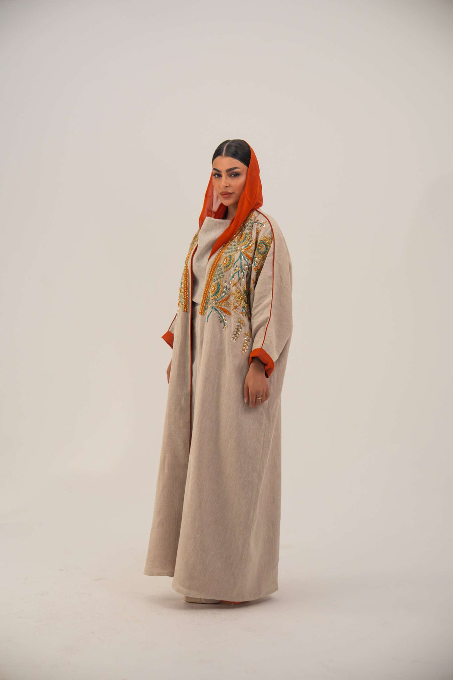 Woman wearing neutral linen Mango Bisht with mango-orange accents and hand-embroidered shoulder panels in earthy and teal tones.