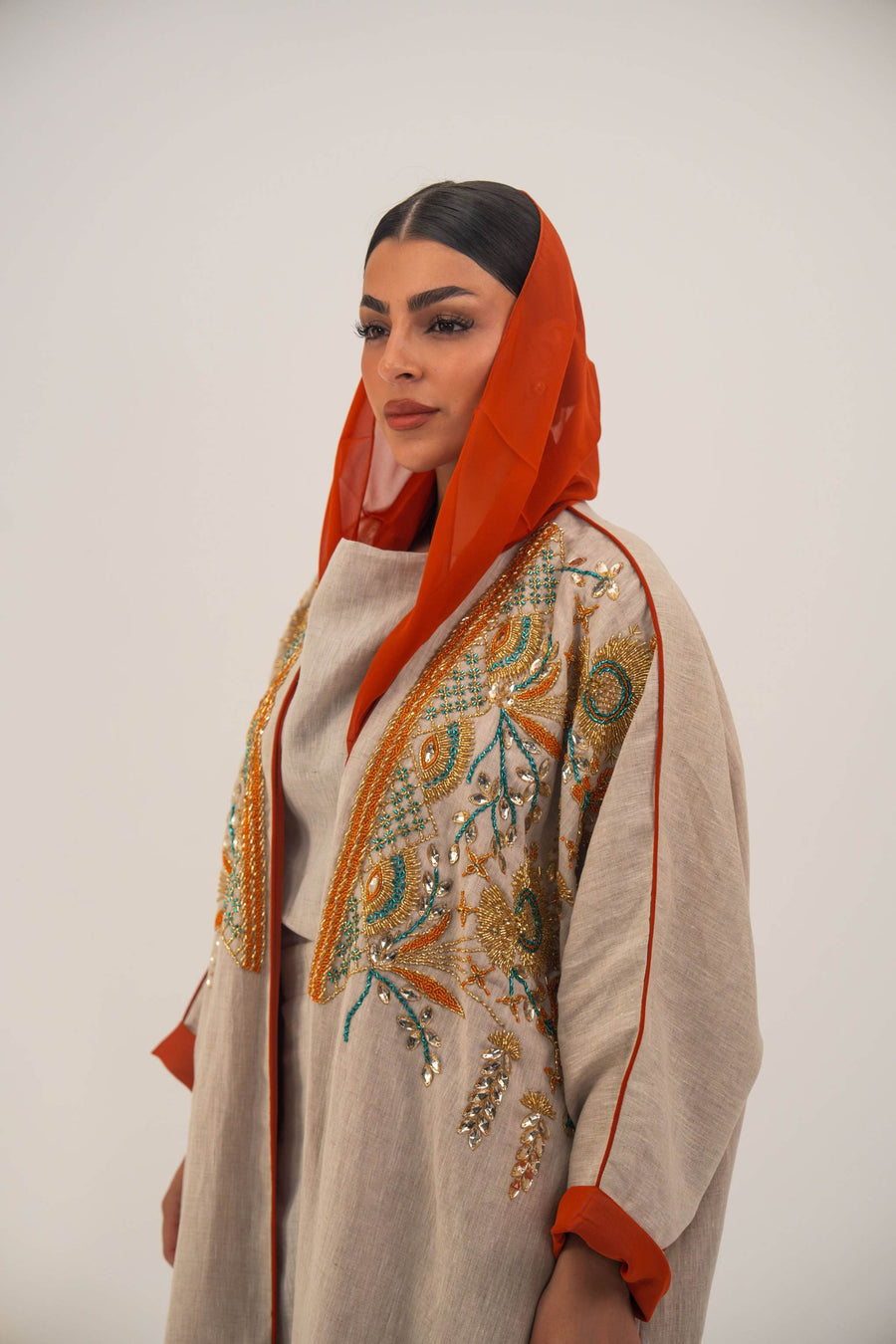 Woman wearing neutral linen Mango Bisht with mango-orange accents and hand-embroidered shoulder panels in earthy and teal tones.