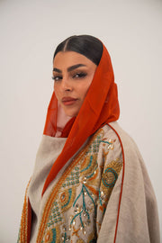 Woman wearing neutral linen Mango Bisht with mango-orange accents and hand-embroidered shoulder panels in earthy and teal tones.