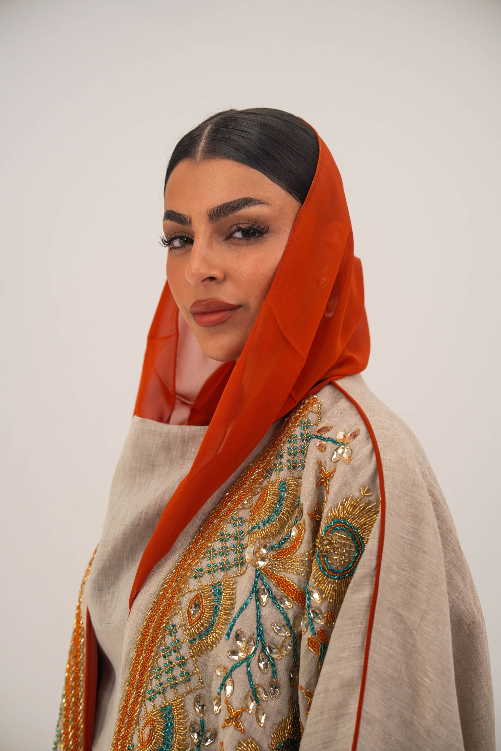 Woman wearing neutral linen Mango Bisht with mango-orange accents and hand-embroidered shoulder panels in earthy and teal tones.