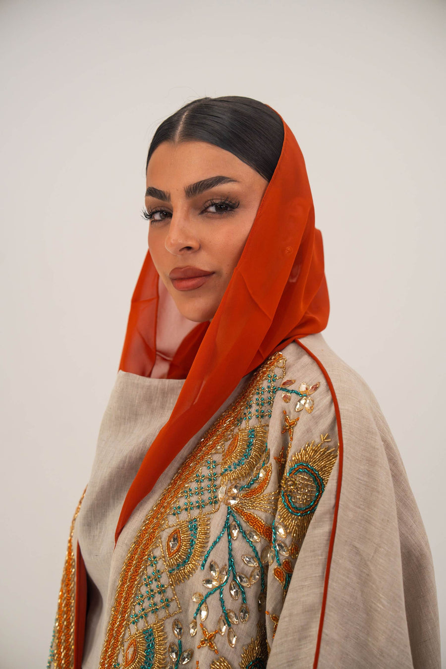 Woman wearing neutral linen Mango Bisht with mango-orange accents and hand-embroidered shoulder panels in earthy and teal tones.