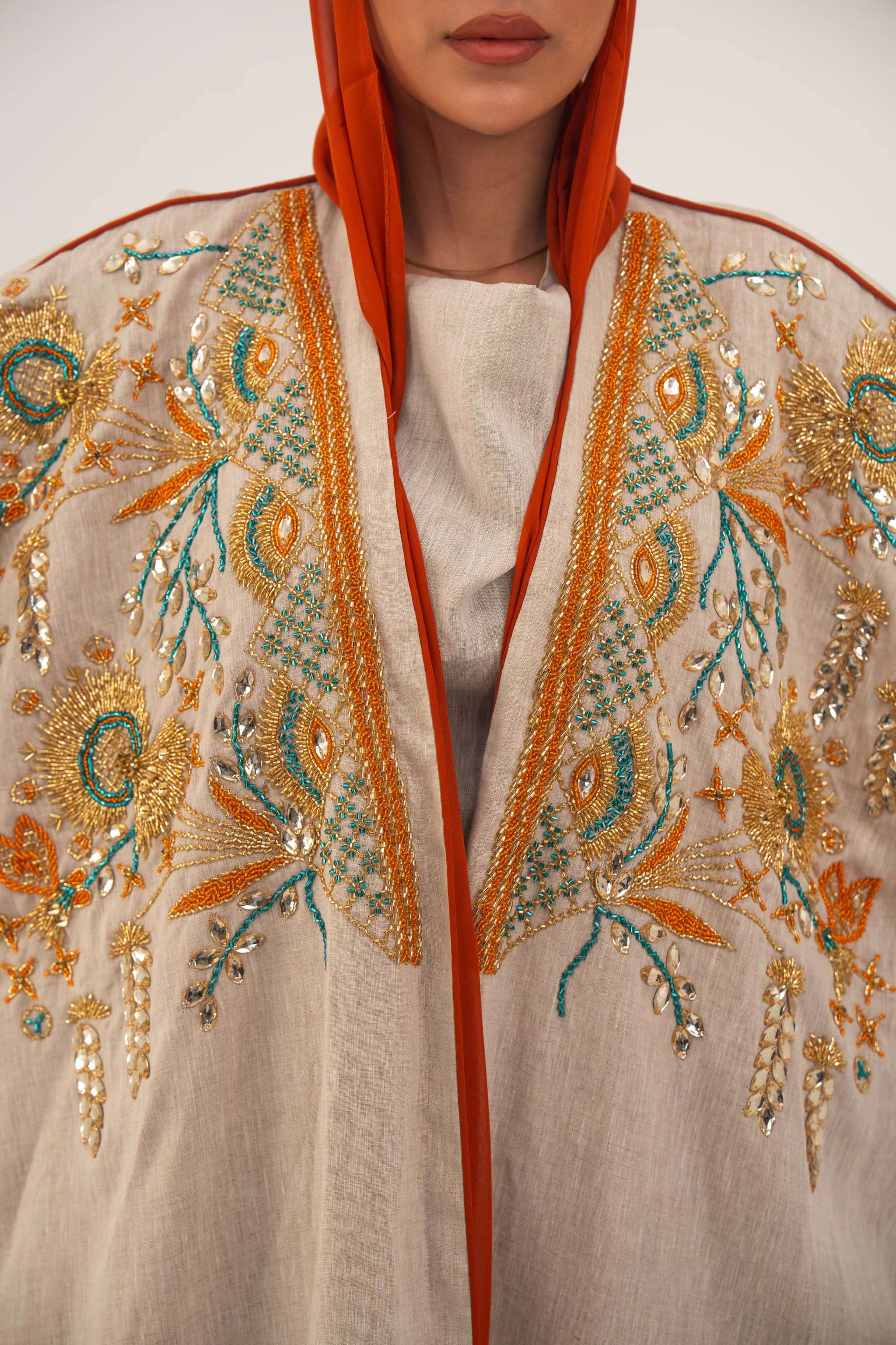 Woman wearing neutral linen Mango Bisht with mango-orange accents and hand-embroidered shoulder panels in earthy and teal tones.