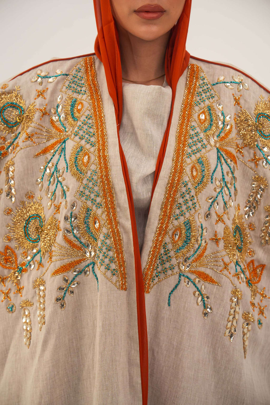 Woman wearing neutral linen Mango Bisht with mango-orange accents and hand-embroidered shoulder panels in earthy and teal tones.