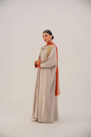 Woman wearing a beige linen-blend abaya with gold and orange beaded embellishments and orange chiffon lining on sleeves and collar