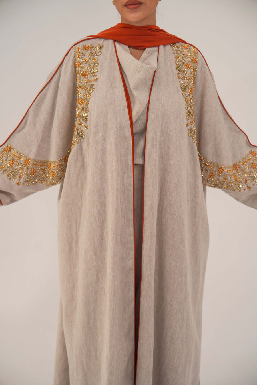 Woman wearing a beige linen-blend abaya with gold and orange beaded embellishments and orange chiffon lining on sleeves and collar