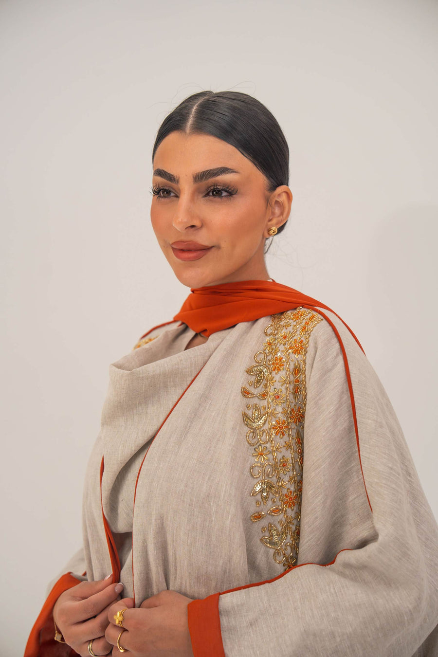 Woman wearing a beige linen-blend abaya with gold and orange beaded embellishments and orange chiffon lining on sleeves and collar
