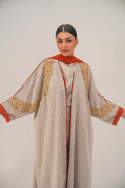 Woman wearing a beige linen-blend abaya with gold and orange beaded embellishments and orange chiffon lining on sleeves and collar