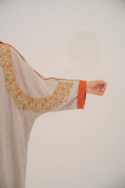 Woman wearing a beige linen-blend abaya with gold and orange beaded embellishments and orange chiffon lining on sleeves and collar