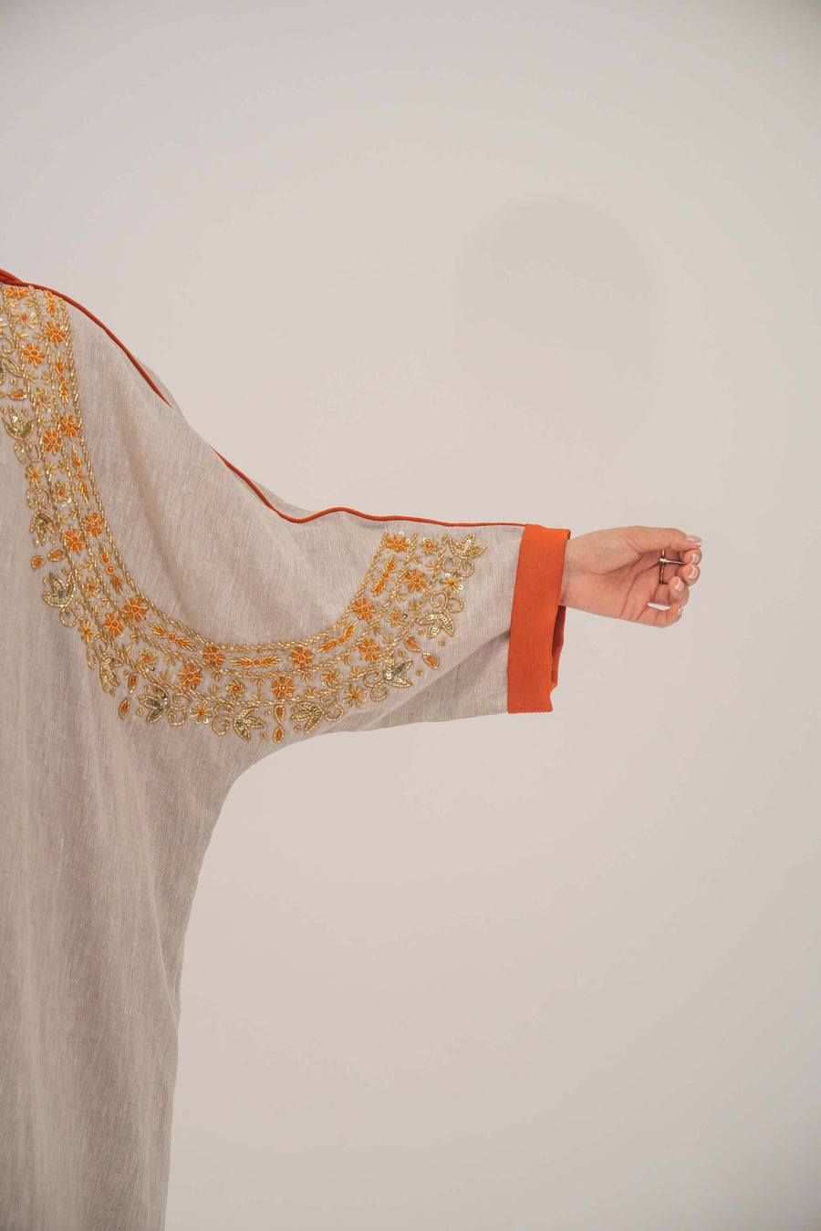 Woman wearing a beige linen-blend abaya with gold and orange beaded embellishments and orange chiffon lining on sleeves and collar