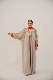 Woman wearing a beige linen-blend abaya with gold and orange beaded embellishments and orange chiffon lining on sleeves and collar