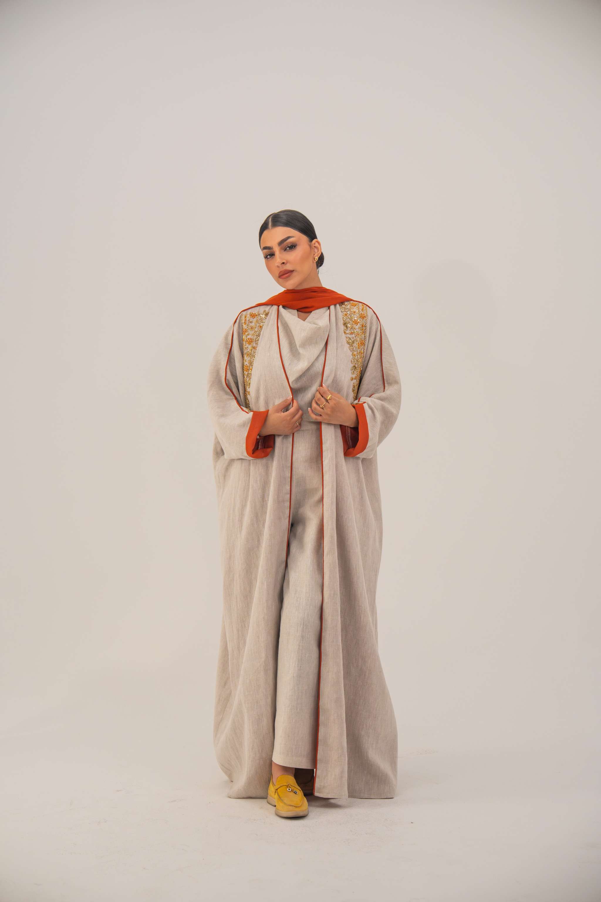 Woman wearing a beige linen-blend abaya with gold and orange beaded embellishments and orange chiffon lining on sleeves and collar