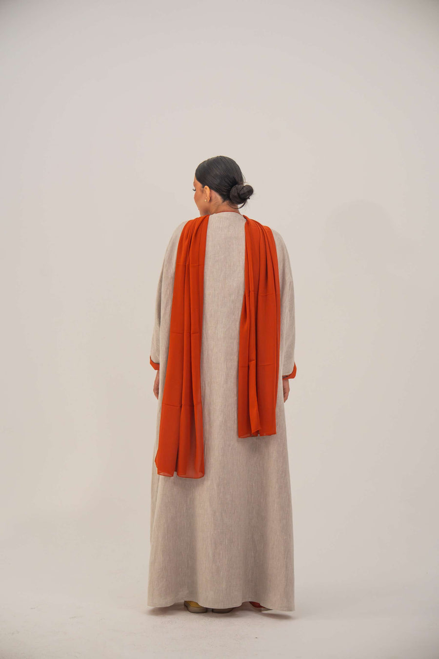 Woman wearing a beige linen-blend abaya with gold and orange beaded embellishments and orange chiffon lining on sleeves and collar
