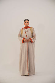 Woman wearing a beige linen-blend abaya with gold and orange beaded embellishments and orange chiffon lining on sleeves and collar