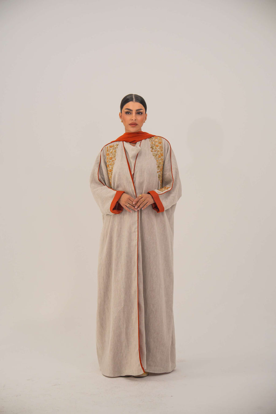 Woman wearing a beige linen-blend abaya with gold and orange beaded embellishments and orange chiffon lining on sleeves and collar