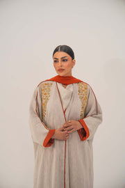Woman wearing beige linen-blend abaya with orange accents and intricate beaded shoulder embellishments