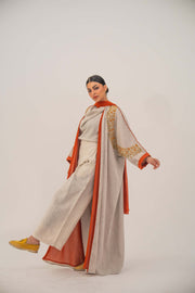 Woman wearing a beige linen-blend abaya with gold and orange beaded embellishments and orange chiffon lining on sleeves and collar