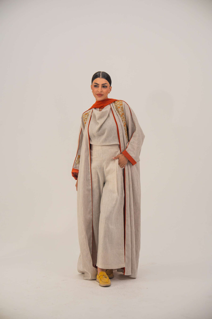 Woman wearing a beige linen-blend abaya with gold and orange beaded embellishments and orange chiffon lining on sleeves and collar