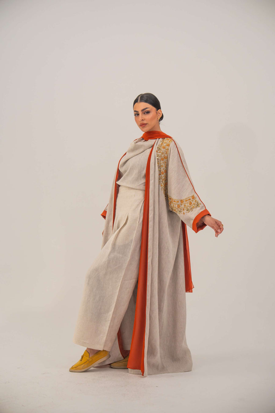 Woman wearing a beige linen-blend abaya with gold and orange beaded embellishments and orange chiffon lining on sleeves and collar